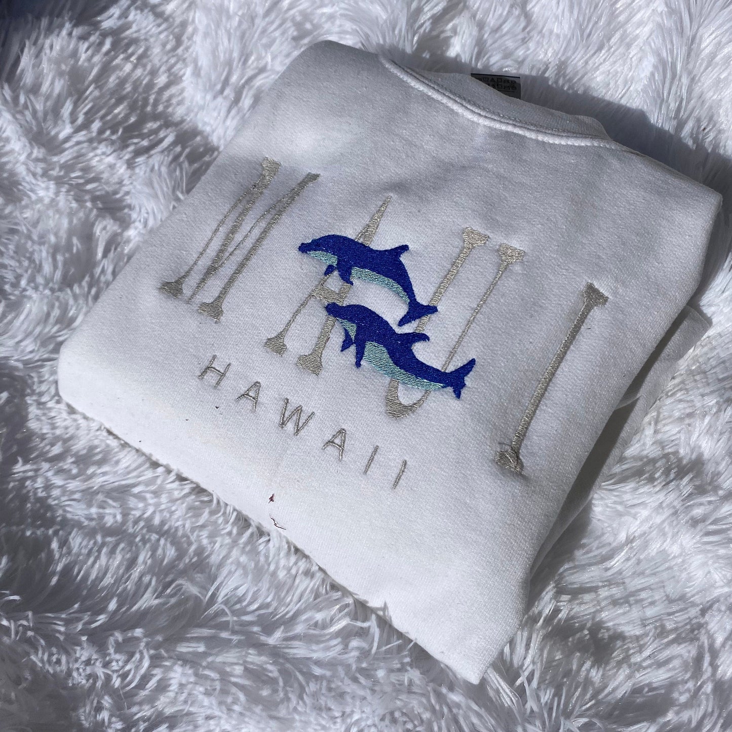 Maui Hawaii embroidered crewneck sweatshirt with blue dolphin design on white fabric.