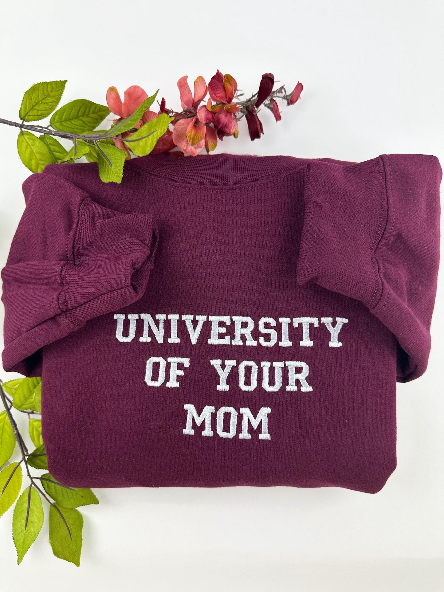 picture of a humorous sweatshirt. the sweatshirt is maroon color with white embroidery of the words “ UNIVERSITY IF YOUR MOM” in capital letters