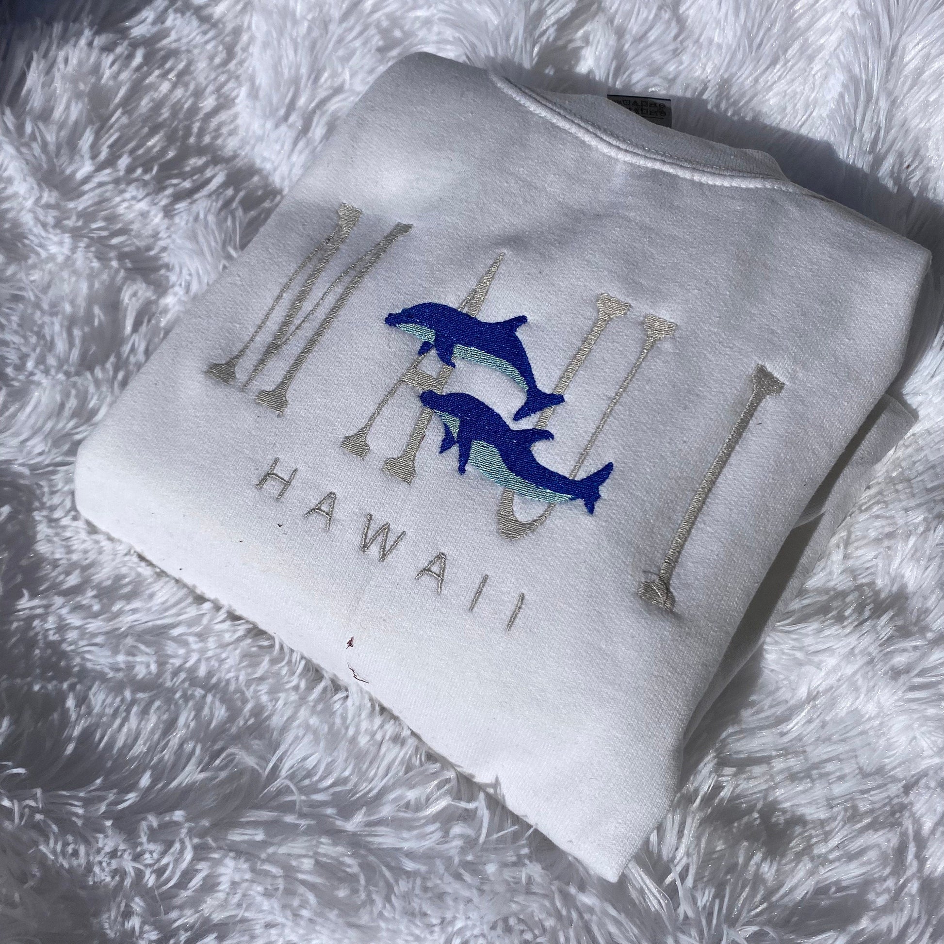 Maui Hawaii embroidered crewneck sweatshirt with blue dolphin design on white fabric.