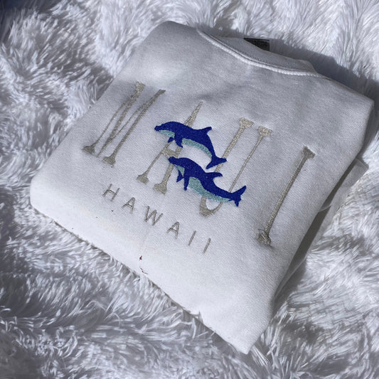 Maui Hawaii embroidered crewneck sweatshirt with blue dolphin design on white fabric.
