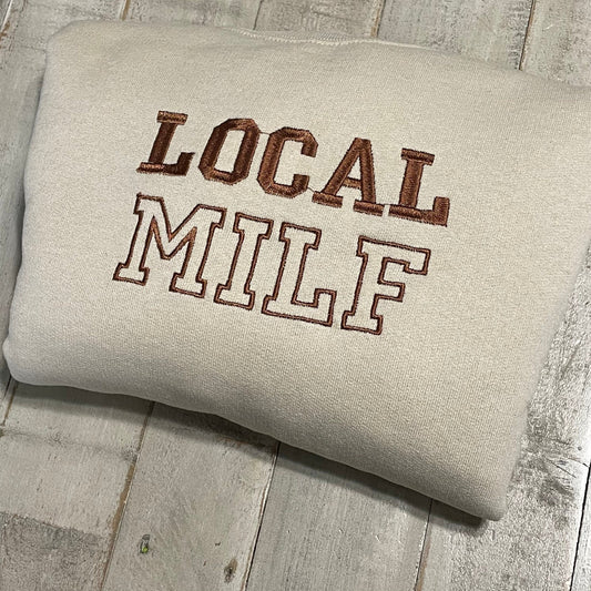 Local Milf Embroidered Crewneck Sweatshirt folded on a wooden surface.