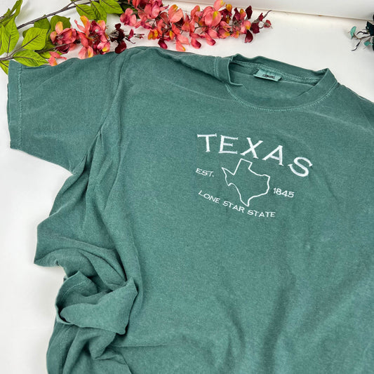 Embroidered Texas Comfort Colors T-shirt with state outline and text design on soft, garment-dyed cotton.