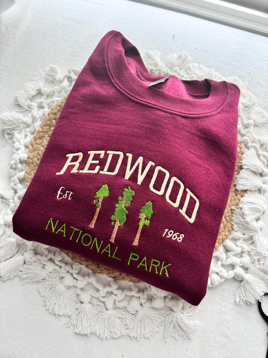 Redwood National Park embroidered burgundy crewneck sweatshirt lying folded on a knitted surface.