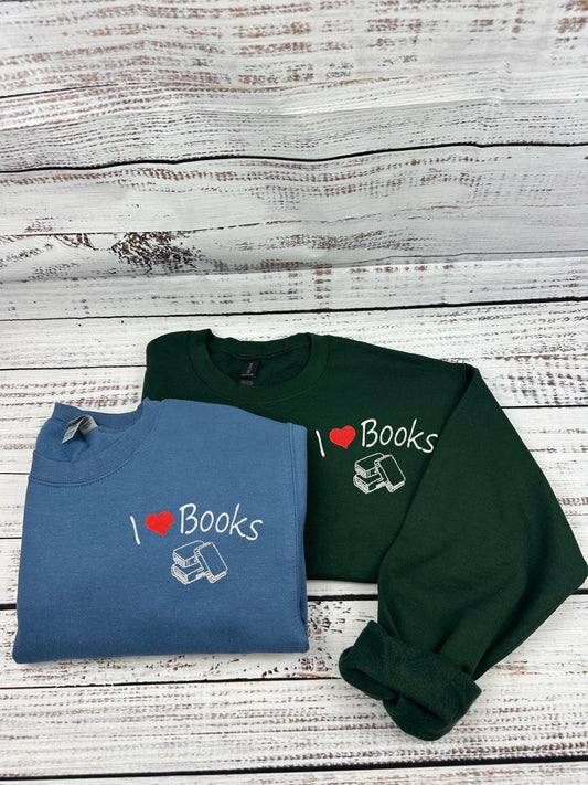 A photo of two sweatshirts, one is green and the other is indigo blue. they both have an embroidery of &quot;I heart books&quot; and an embroidery of 3 books under it. The heart is just an embroidery in the shape of a heart. The thread is white and red