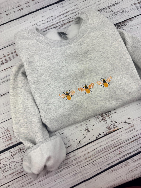 Embroidered bumble bee crewneck sweatshirt on a white wooden background.