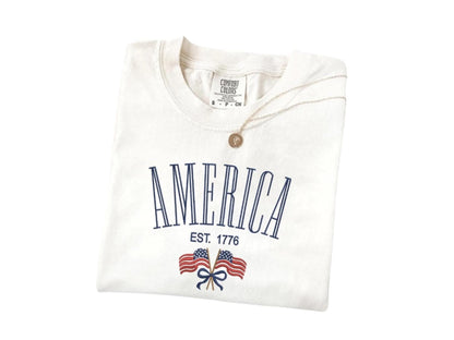 America Est. 1776 T-Shirt in ivory color, featuring vintage design with double flags, soft Comfort Colors cotton, perfect for patriotic celebrations.