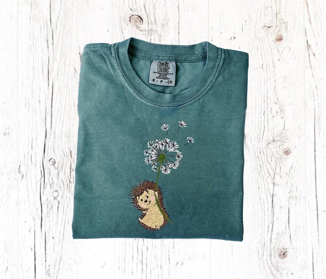 Embroidered hedgehog shirt with dandelion on green Comfort Colors tee, perfect for nature lovers.